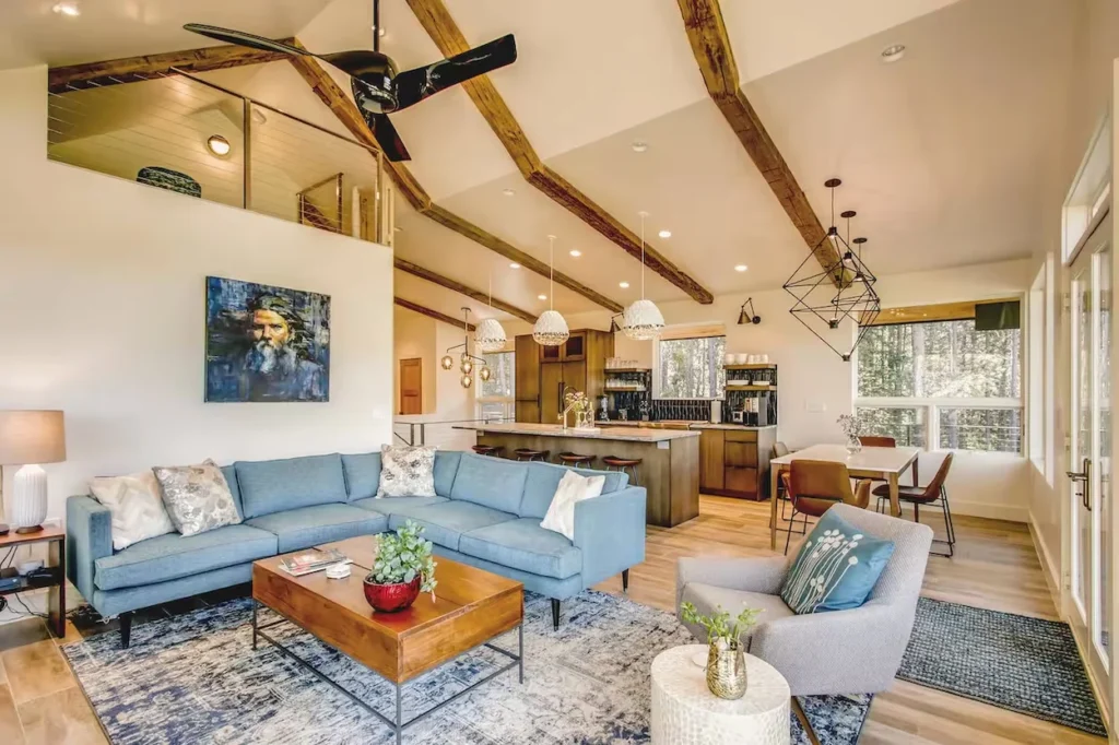 Open-concept cabin living room with blue sectional and vaulted wood-beam ceilings