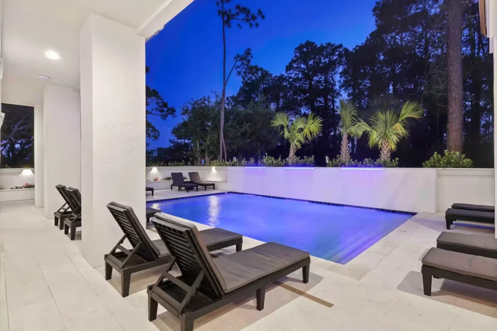 Illuminated backyard swimming pool with lounge chairs at dusk