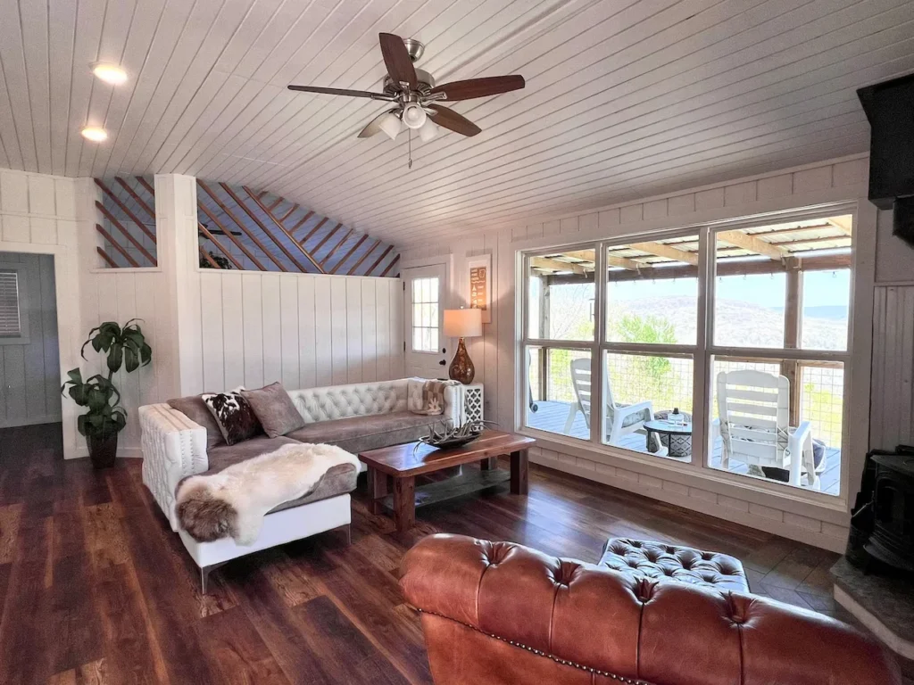 Mountainburg cabin living room with a white sectional sofa, leather chair, and large viewing windows