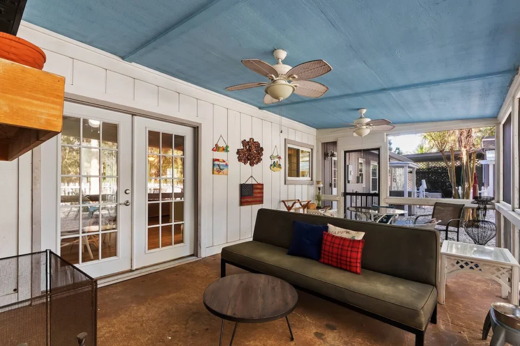 Screened-in porch with a blue painted ceiling, green sofa, and ceiling fans