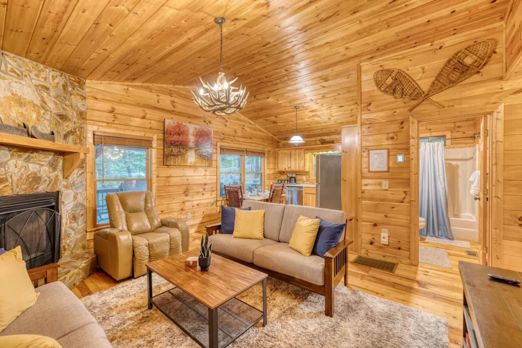Cabin living room with wood walls, an antler chandelier, sofas, and a stone fireplace
