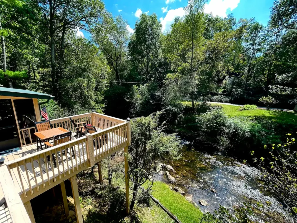 Elevated cabin porch deck overlooking a rocky creek surrounded by green trees