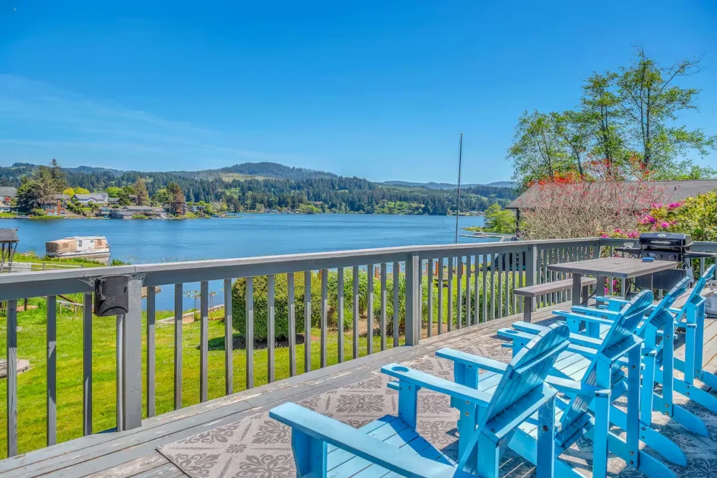 Wooden deck with blue Adirondack chairs overlooking a wide lake and forested hills