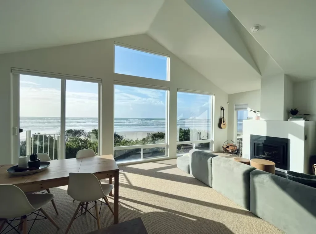Bright modern living room with large glass windows overlooking a sandy beach and ocean waves