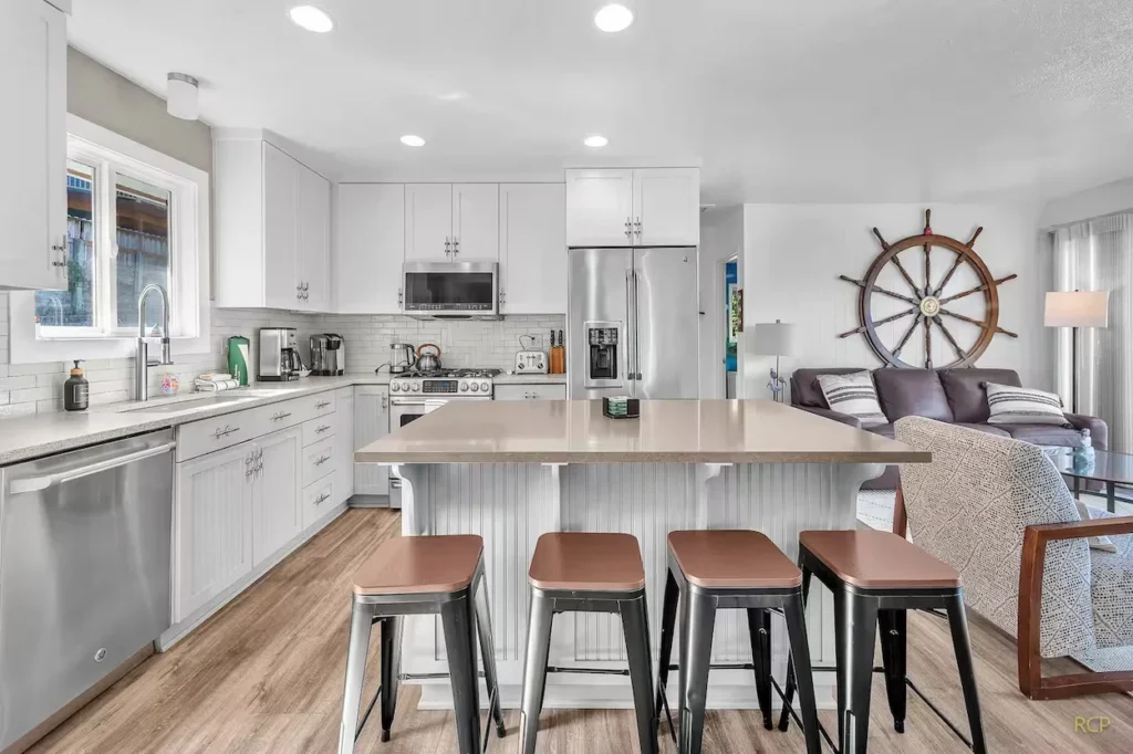 Bright modern kitchen with white cabinets, stainless steel appliances, large island with stools, and nautical decor