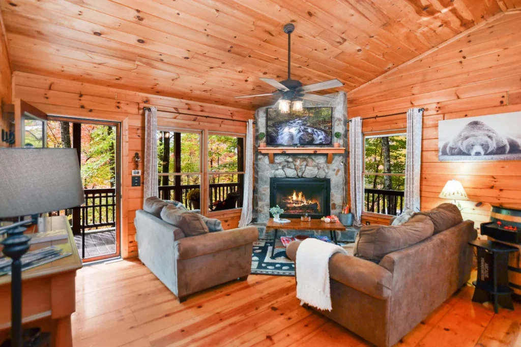 Cabin living room with wood paneled walls, two brown sofas, and a lit stone fireplace