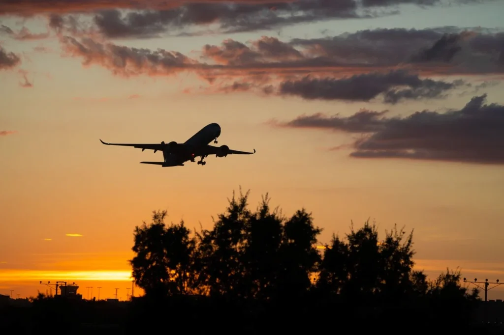 Silhouette of an airplane taking off against a bright orange sunset sky