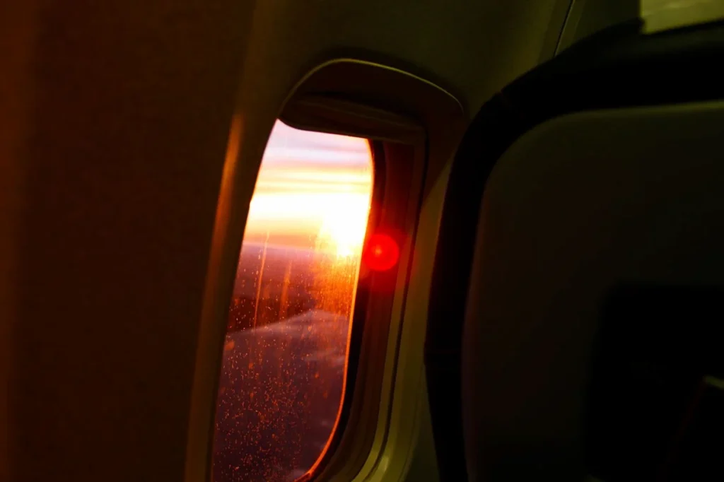 Bright sunset glowing through an airplane passenger window with lens flare