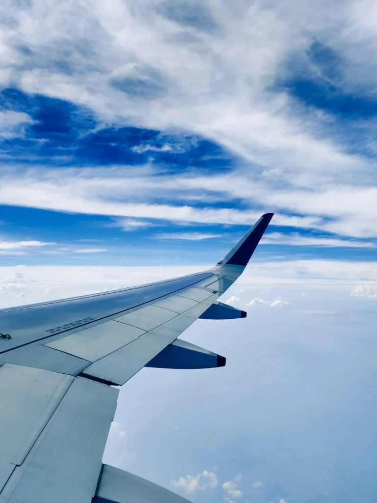 An airplane wing with a sharklet tip flying high above the clouds under a bright blue sky