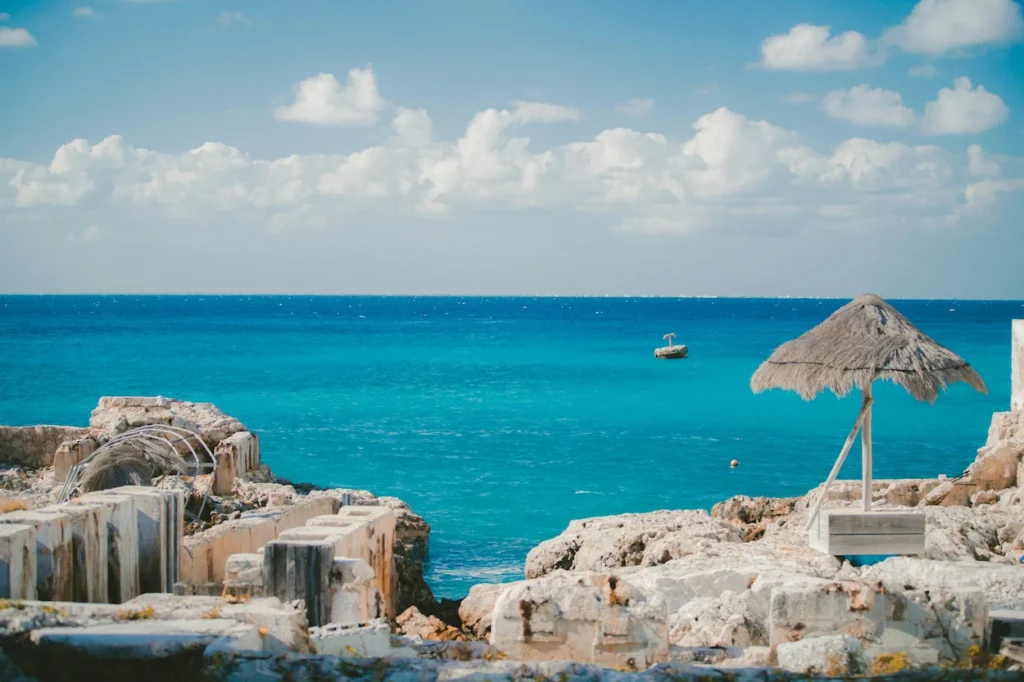 Rocky limestone coastline overlooking the turquoise ocean water with a straw umbrella in Cozumel, Mexico