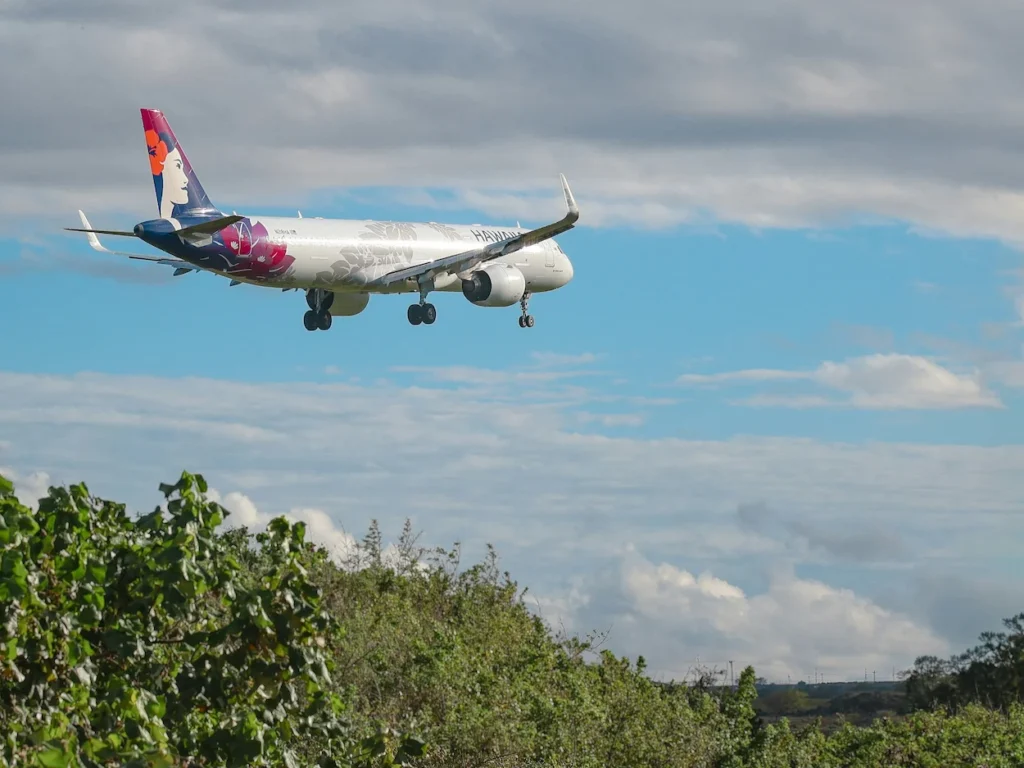 Hawaiian Airlines aircraft flying low over green trees to land