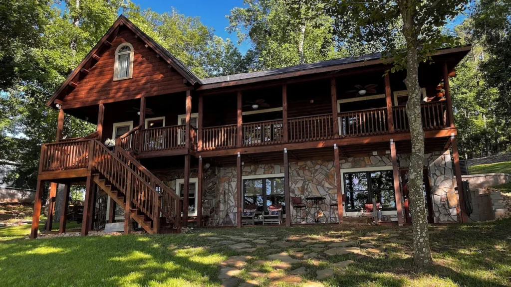 Two story log cabin with a stone lower level, wooden balconies, and a grassy yard