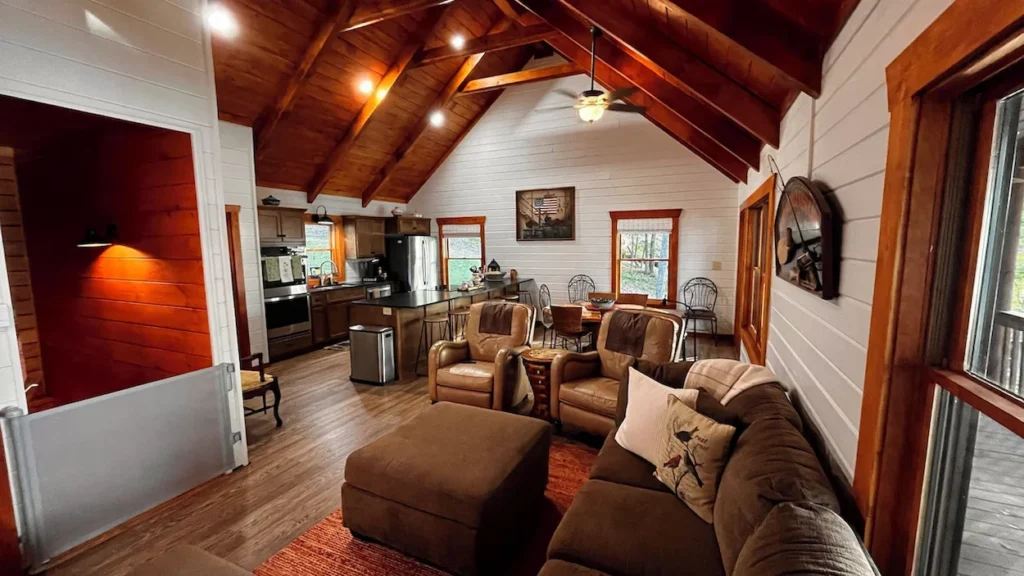 Cabin interior showing an open living room with brown furniture, a dining table, and a kitchen