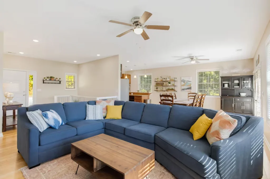 Bright open living room featuring a large blue sectional couch, wooden coffee table, and an attached dining space