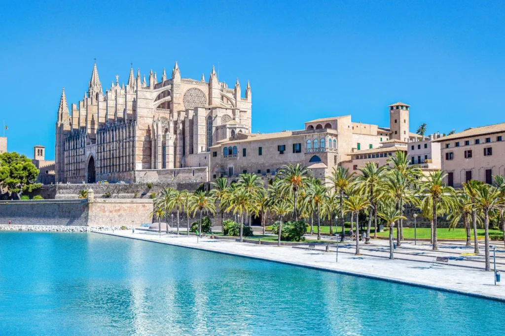 Palma Cathedral rising above a palm-lined promenade and clear blue water in Mallorca, Spain