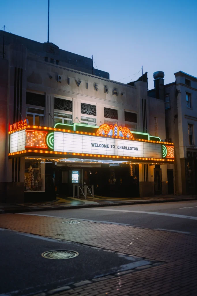 The glowing neon marquee of the Riviera Theater reading welcome to Charleston at dusk