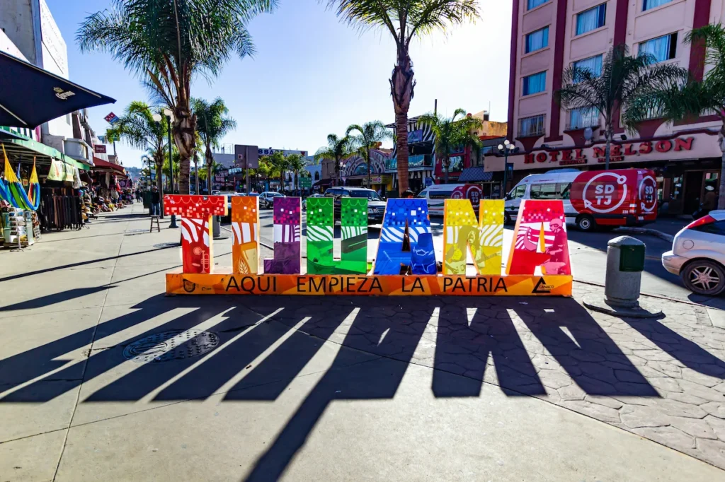Colorful Tijuana sign with the slogan "Aqui Empieza La Patria" on a city sidewalk