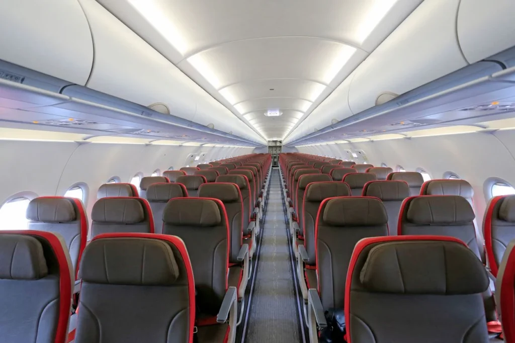 Empty airplane cabin aisle showing rows of grey economy seats with red trim accents