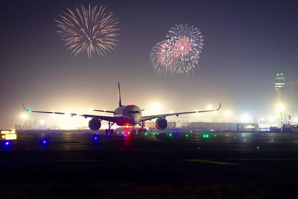 An Airbus A350 passenger airplane on a lit runway with fireworks overhead