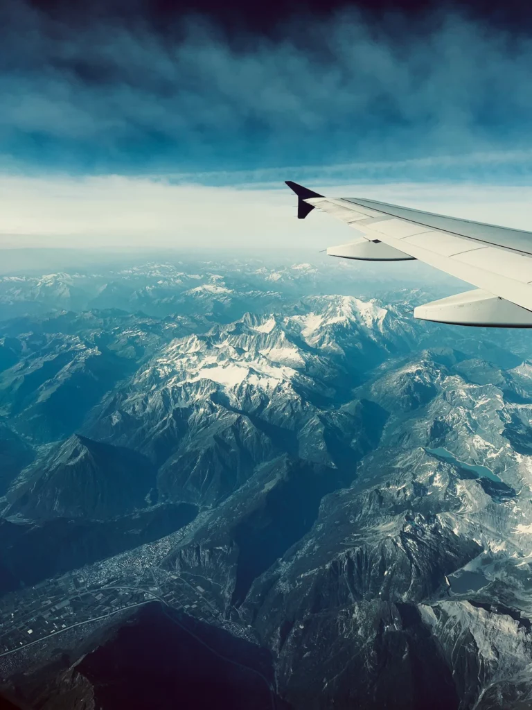 View from an airplane window showing a wing flying high above snow-capped mountain peaks