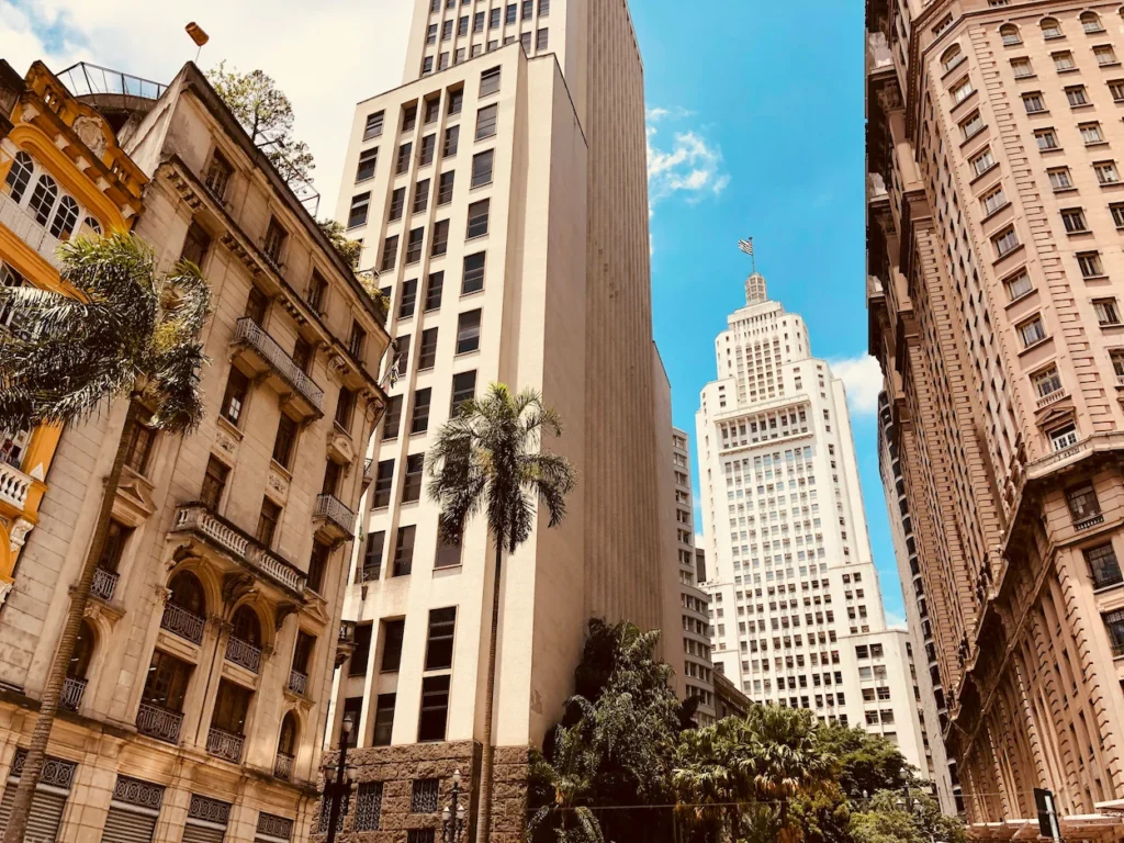 Classic skyscrapers and palm trees framing the white Altino Arantes tower under a blue sky in São Paulo