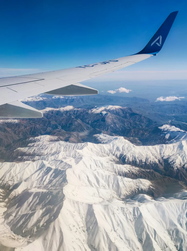 An AJet airplane wing flying over snow covered mountain peaks