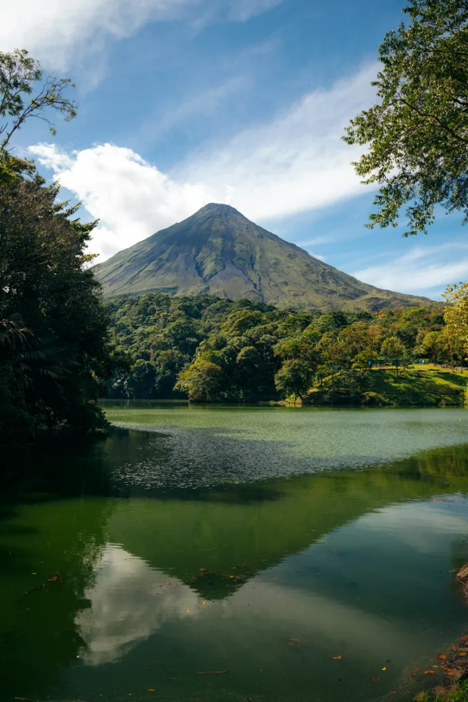 Arenal Volcano peak reflecting on a green lake surrounded by tropical forest
