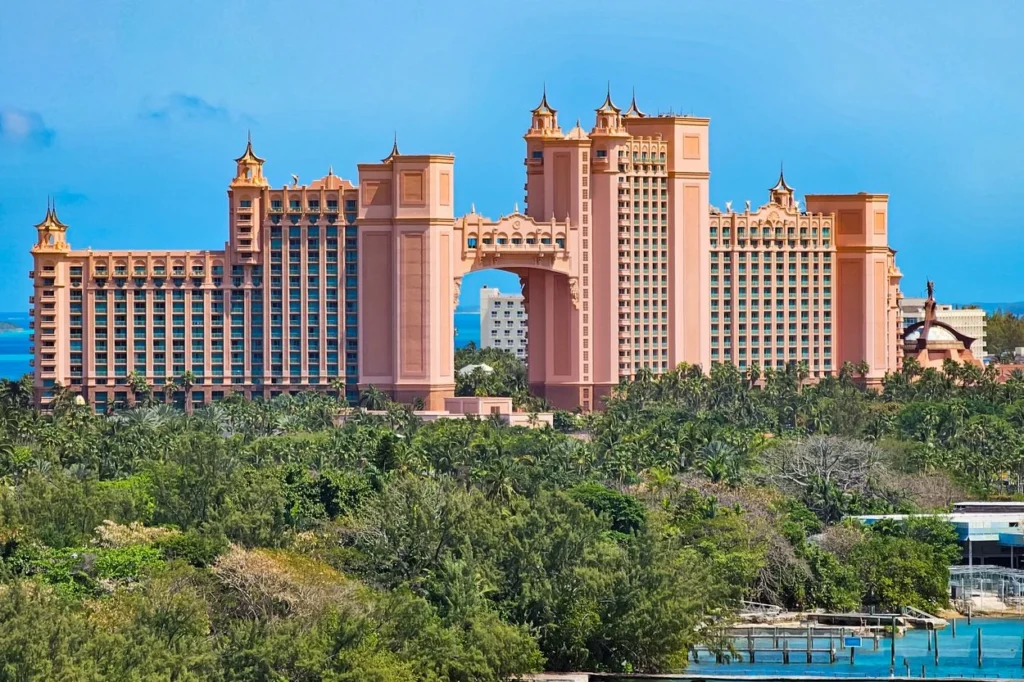 The pink towers of the Atlantis Paradise Island resort rising above lush green trees under a clear blue sky