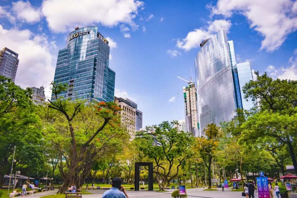 Modern glass skyscrapers rising behind the trees of Ayala Triangle Gardens in Makati