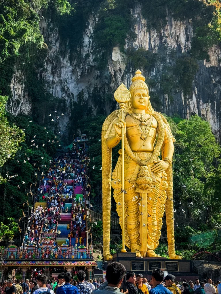 Giant golden Lord Murugan statue standing next to colorful rainbow stairs at Batu Caves