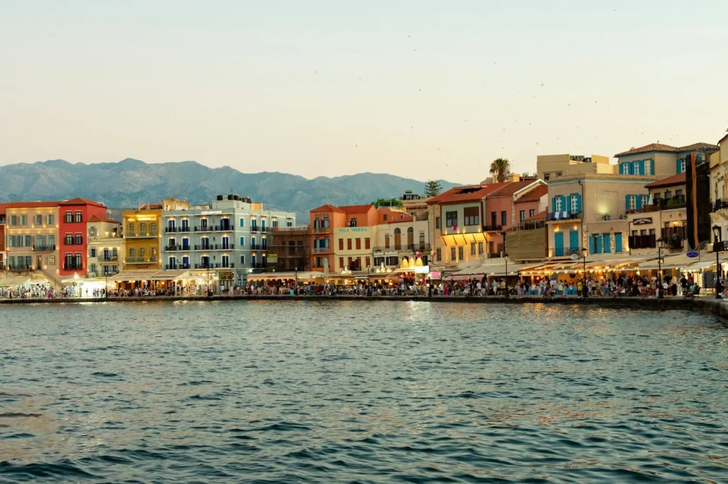 Colorful historic buildings lining a waterfront harbor at dusk with mountains in the background