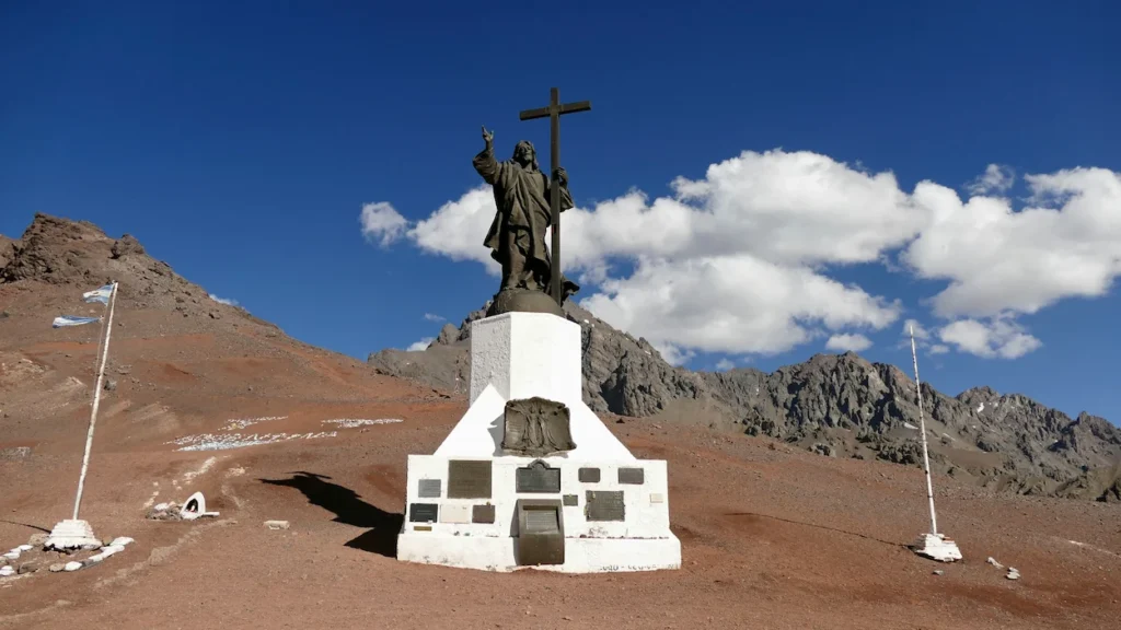 Jesus statue with a cross on a white stone pedestal in the rocky Andes mountains