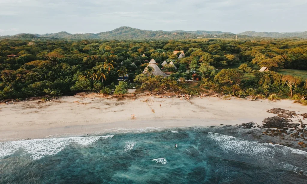 Aerial view of thatched-roof cabins at a coastal eco-resort on a tropical beach in Costa Rica