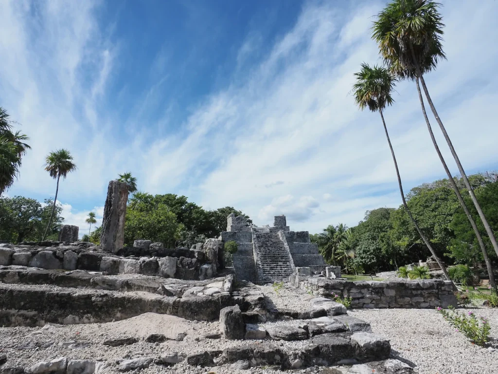 Ancient stone pyramid structure at El Meco Mayan ruins in Cancun surrounded by palm trees