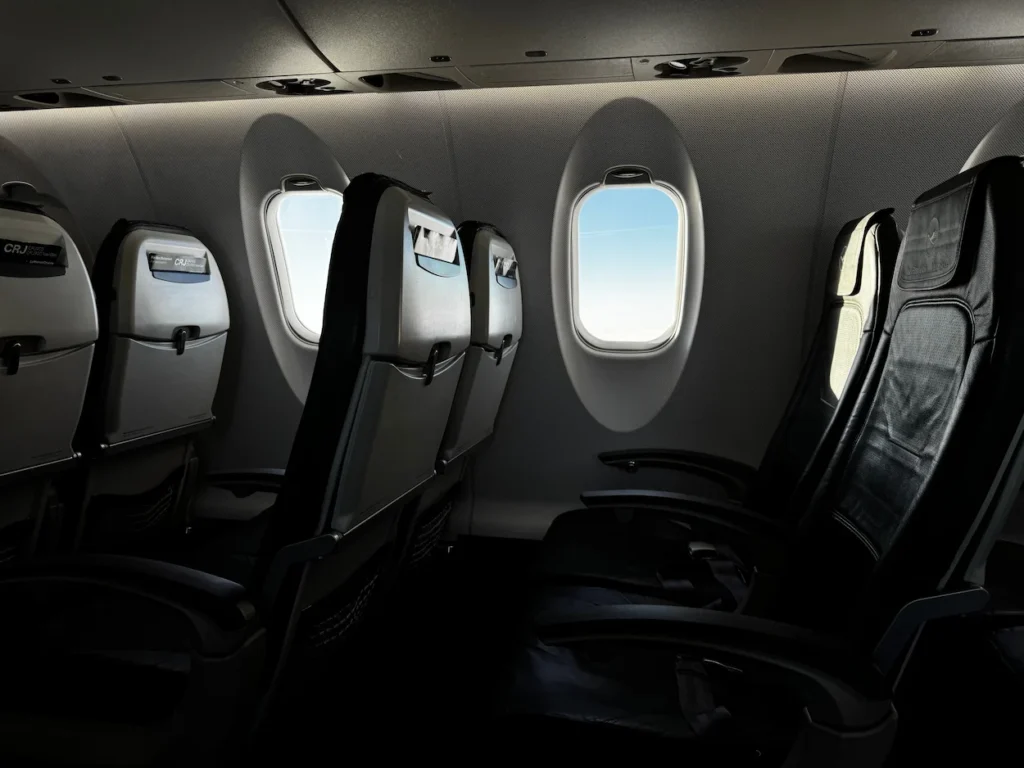 Empty grey airplane cabin interior featuring rows of leather seats with CRJ safety placards next to windows