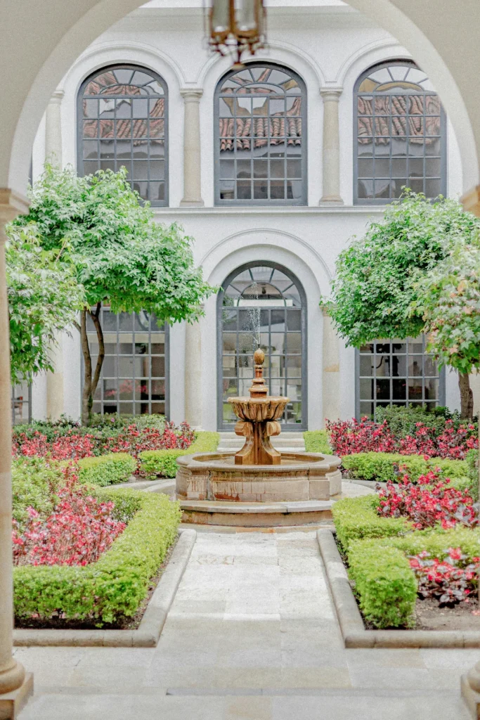 Central stone water fountain in a courtyard garden with flowers and arched windows at Museo Botero