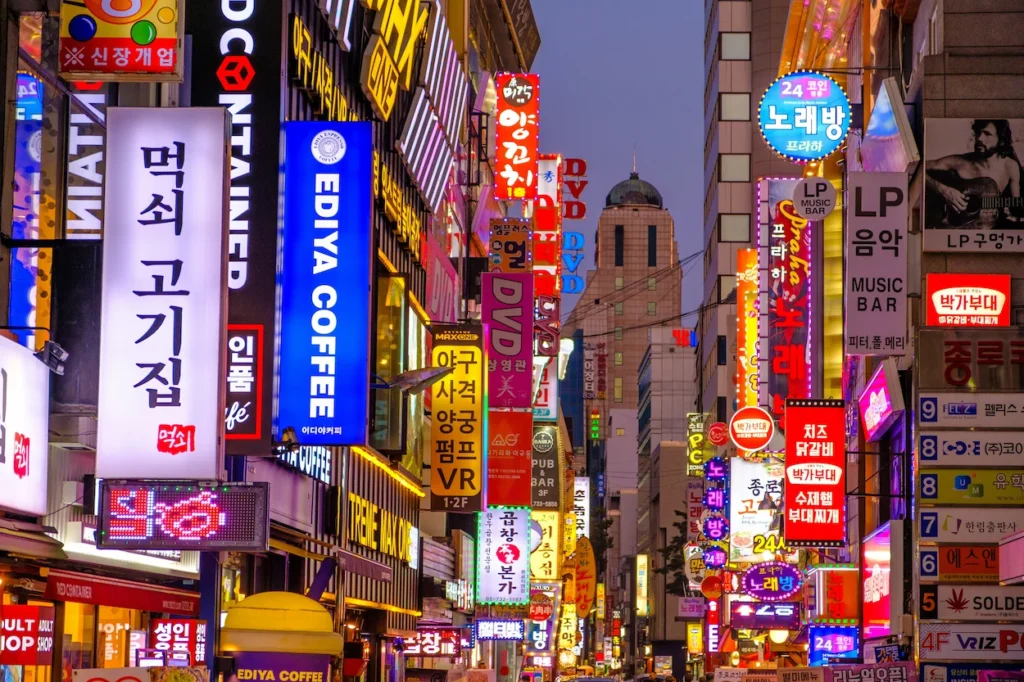 Densely packed vertical neon and LED shop signs along a narrow street in Myeongdong, Seoul