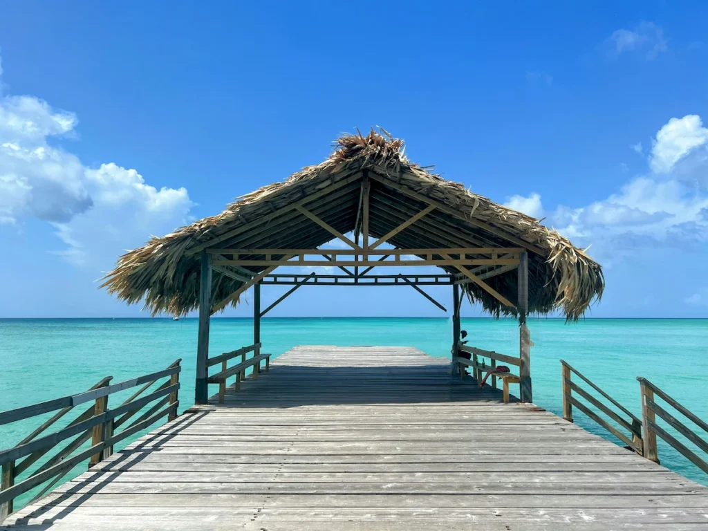 Wooden boardwalk leading to the thatched-roof Pigeon Point Jetty over turquoise water