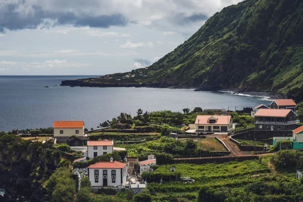 Coastal village with orange-roofed houses below a green volcanic mountain on São Jorge Island, Azores