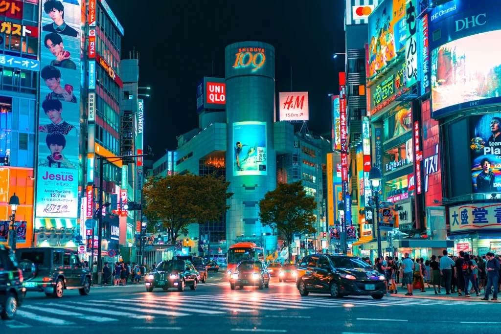Shibuya 100 building surrounded by neon signs, billboards, and traffic at a crosswalk in Tokyo at night