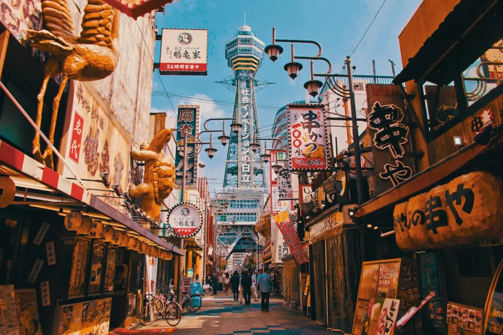 Tsutenkaku Tower framed by vibrant restaurant signs and shops along a street in Shinsekai, Osaka