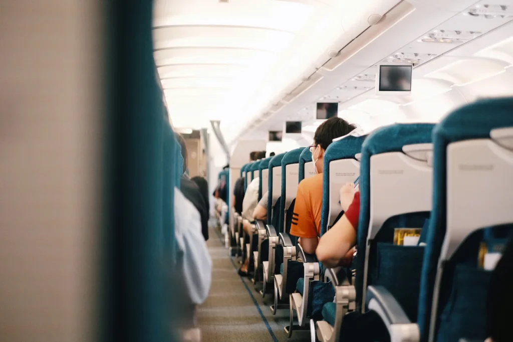 View down an airplane aisle showing passengers seated in teal economy class seats