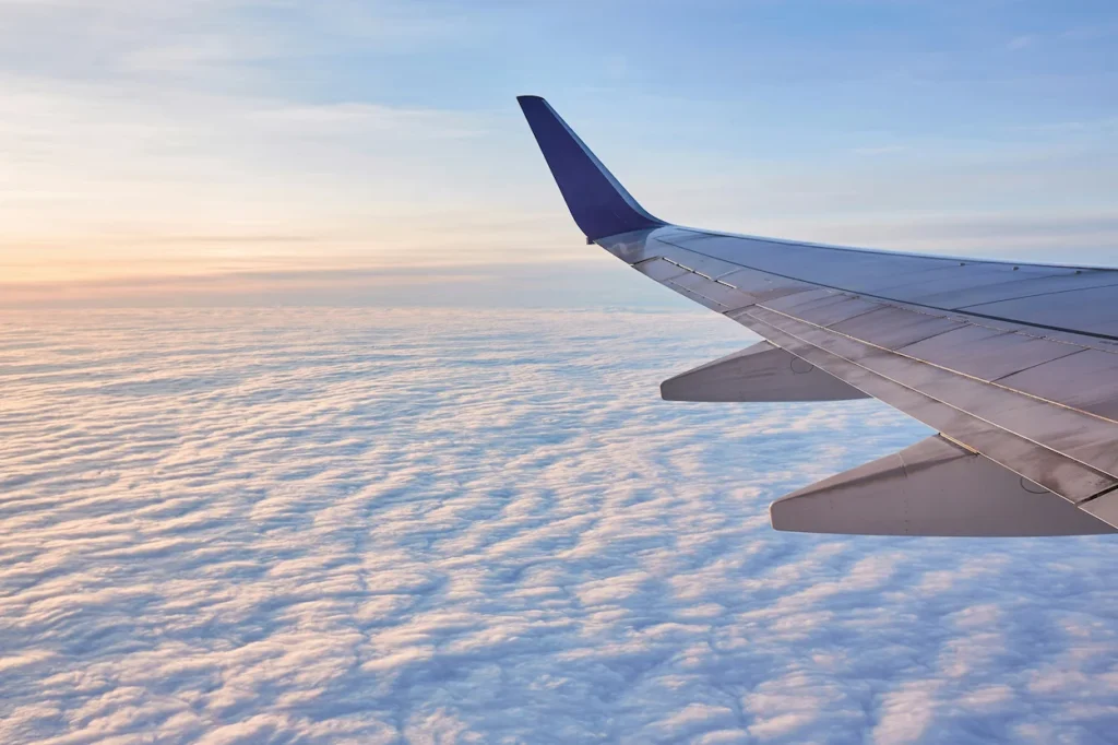 An airplane wing with a blue wingtip cruising high above a thick layer of clouds at sunset
