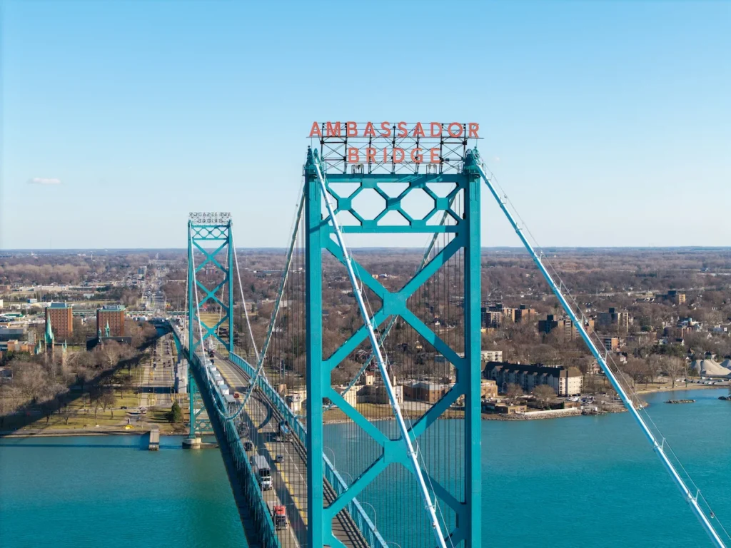 Teal suspension tower of the Ambassador Bridge crossing over the blue Detroit River under a clear sky