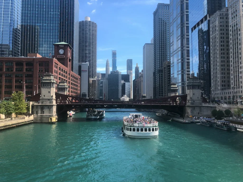 Tour boat cruising down the turquoise Chicago River flanked by downtown skyscrapers