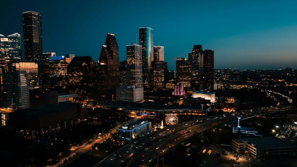 An elevated night view of the illuminated downtown Houston skyline and busy highway traffic