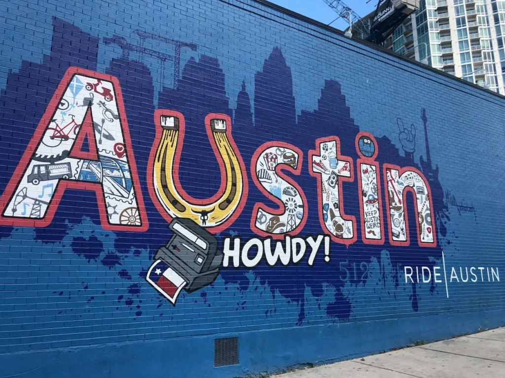Colorful Howdy from Austin mural on a blue brick wall downtown