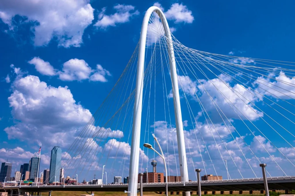 Margaret Hunt Hill Bridge white arch with the Dallas skyline under a cloudy blue sky