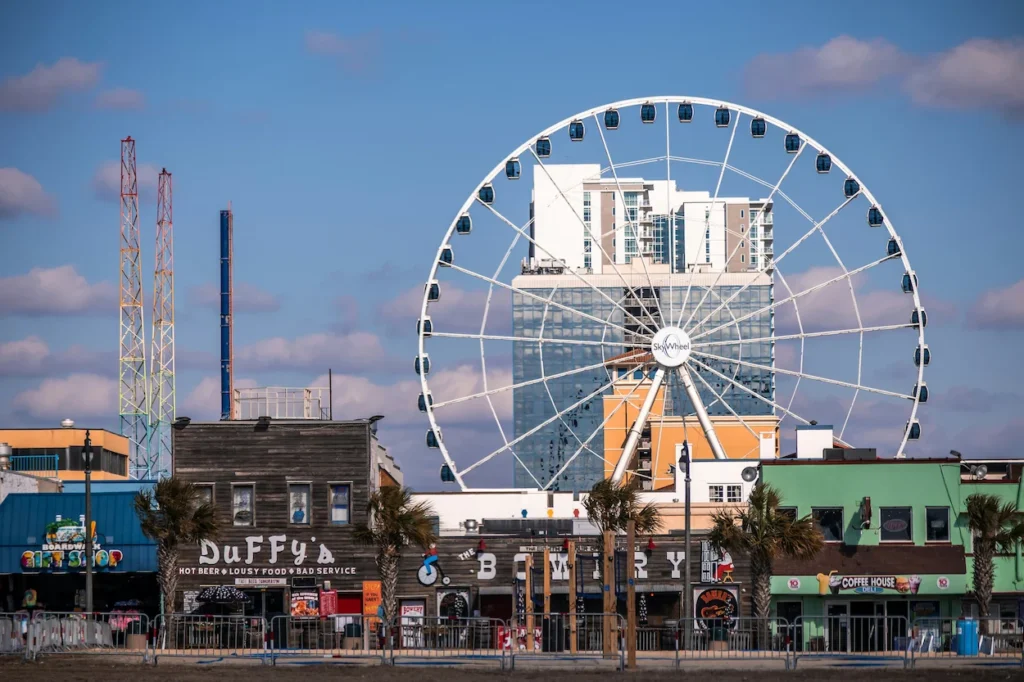 Myrtle Beach SkyWheel rising behind Duffy's and storefronts under a blue sky