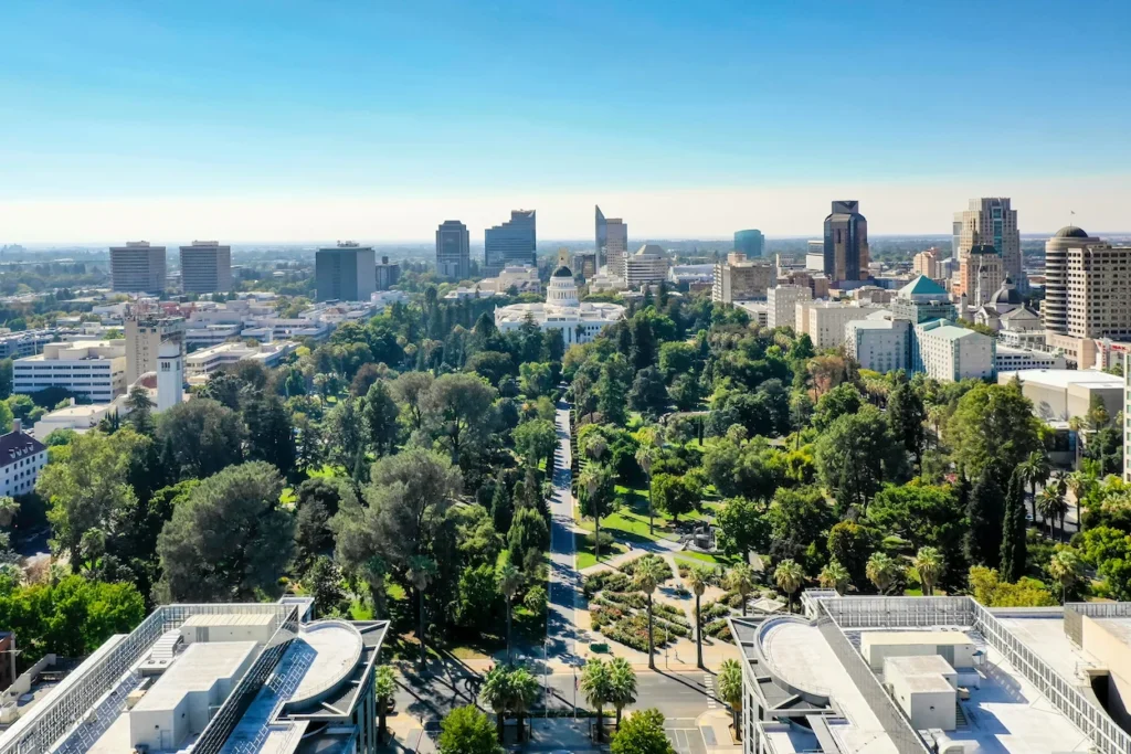 Aerial view of the California State Capitol building surrounded by trees and the Sacramento skyline